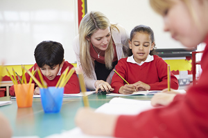 Female Teacher Helping Young School Girl And Boy With Writing